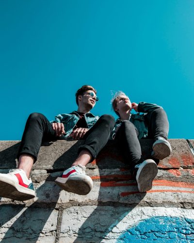 pexels-photo-1019771-1019771 Two young people sitting on a stone wall under a vibrant blue sky, enjoying a sunny day together.